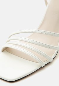 Λευκό σανδάλι με τρεις λεπτές ραμμένες λουρίδες κατά μήκος του ποδιού και τετράγωνο σχέδιο στα δάχτυλα.