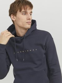 Mørkeblå hoodie lavet af blødt stof, med et gyldent logo print "JACK & JONES" foran og en kengurulomme. Justerbar snoretræk i hætten.
