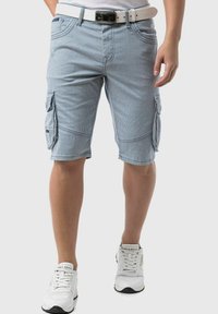 Shorts cargo rayés bleus et blancs avec de multiples poches, un devant plat et des coutures contrastées. Portés avec une ceinture blanche et des baskets blanches.