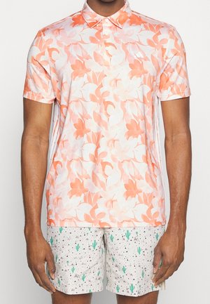 Polo à manches courtes en crème avec un motif floral corail, fabriqué dans un tissu léger. À associer avec un short clair orné de cactus verts et de motifs de montagnes noires.