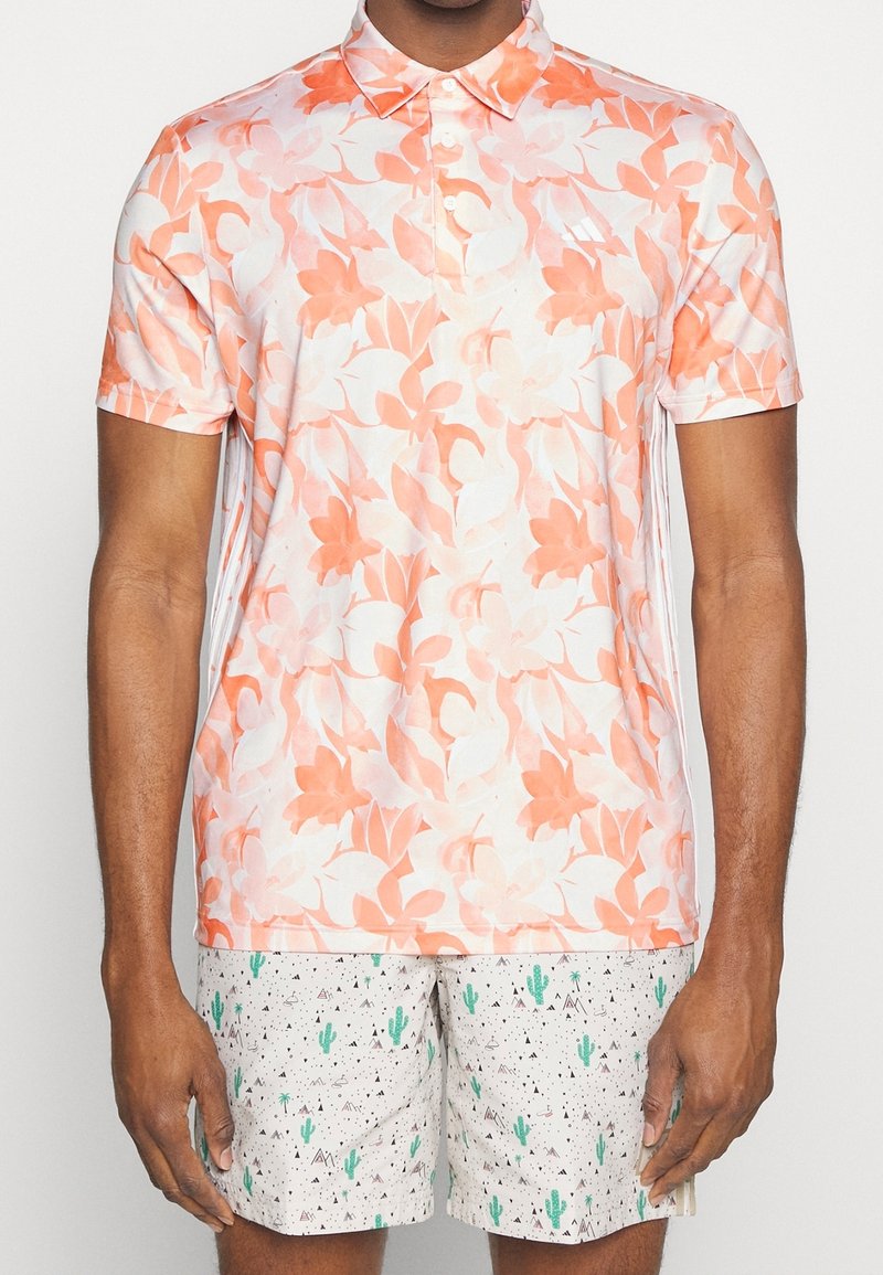 Polo tričko s krátkým rukávem v krémově a korálově barevném květinovém vzoru, vyrobené z lehkého materiálu. Kombinujte s lehkými šortkami s motivem zelených kaktusů a černých hor.