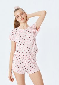 Ensemble de vêtements de détente rose clair avec un petit motif à pois rouge. Haut à manches courtes avec col rond, associé à un short avec un ourlet festonné.