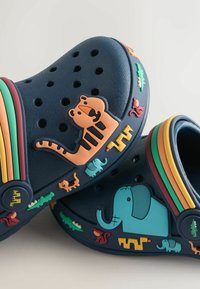 Zoccoli in gomma blu navy con decorazioni a forma di animali in arancione, verde e giallo. Fori per la ventilazione. Forma arrotondata.