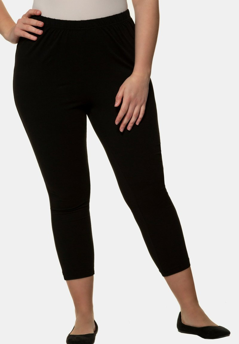 Leggings neri alla caviglia con una fascia elastica in vita, realizzati in un tessuto liscio. Design aderente, senza motivi o dettagli visibili.