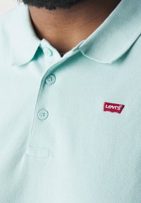 Polo vert menthe clair avec un motif texturé, doté d'un col, de trois boutons et d'un patch logo Levis rouge sur la poitrine.
