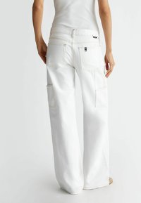 Białe spodnie cargo wykonane z denimu, z szerokimi nogawkami, wieloma kieszeniami i kontrastowymi przeszyciami. W pasie znajduje się mała metka z logo marki.