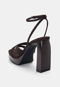 Brown suede high-heeled sandal with a thick block heel and cross-strap design. Features a textured heel and adjustable ankle strap.