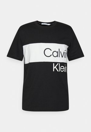 Sort og hvid kortærmet t-shirt med vandrette striber og mærkenavnet "Calvin Klein" i fed typografi.
