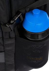 Zaino nero con una tasca in rete che contiene una borraccia nera con un coperchio blu. Cinghie regolabili e fibbia visibili. Materiale testurizzato.