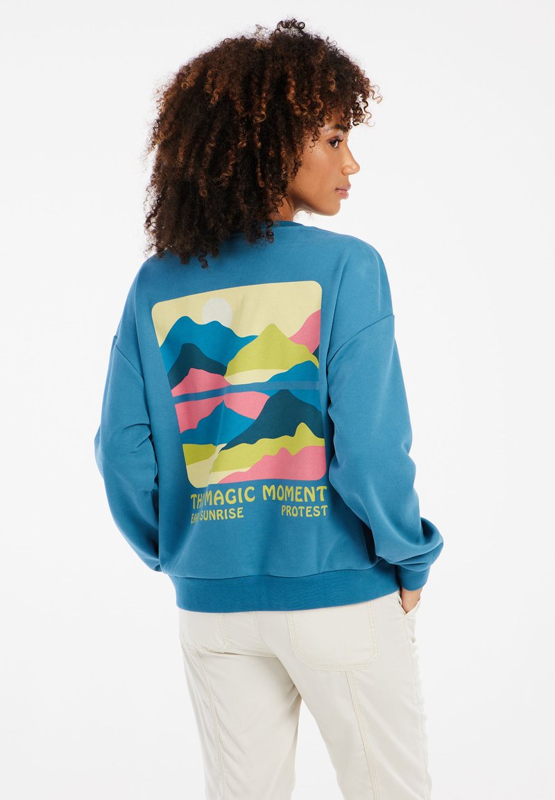 Modrá mikina so zaujímavým grafickým motívom hory na chrbte. Vyrobená z mäkkej tkaniny s voľným strihom a elastickými manžetami.