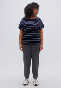 Μπλούζα με μπλε και λευκές ρίγες, άνετη εφαρμογή και κοντά μανίκια, συνδυασμένη με γκρι παντελόνι. Το σύνολο ολοκληρώνεται με λευκά αθλητικά παπούτσια.