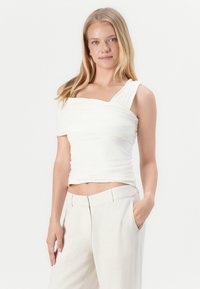 Top blanco ajustado con un diseño fruncido y estilo de un solo hombro. Hecho de una tela suave, combinado con pantalones sueltos de color claro.