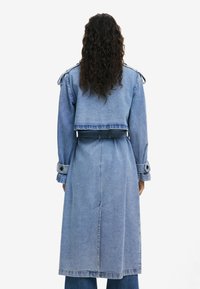 Denim-Trenchcoat mit einem verkürzten oberen Abschnitt, langen Ärmeln, tailliertem Gürtel, doppelreihigen Knöpfen und einem hellblauen Waschung.