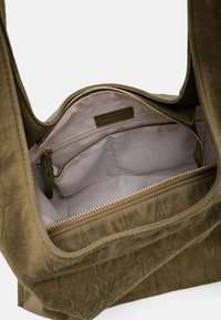 Schoudertas van olijfgroen suède met een ritssluiting aan de bovenkant, binnenvakken en een textuurrijke buitenkant. Voorzien van een rits met goudkleurige sluiting.