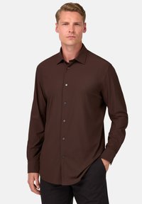 Ruda ilgomis rankovėmis marškiniai su klasikinėmis apykaklėmis, turintys mygtukų uždarymą ir lygų audinį. Derinama su tamsiomis kelnėmis, pabrėžiančiomis tvarkingą išvaizdą.