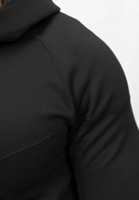 Haut de sport noir avec un design ajusté. Fabriqué en tissu lisse et extensible, il présente une zone d'épaule sans coutures et de subtils détails de couture.