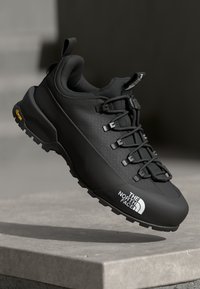 Black hiking shoe with a textured upper, lace closure, and rugged outsole. Features branding and a durable rubber tread for traction.