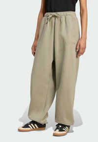 Større beige joggers med snoretræk i taljen, sidelommer og subtil "adidas" broderi, parret med sorte og cremefarvede sportssko.