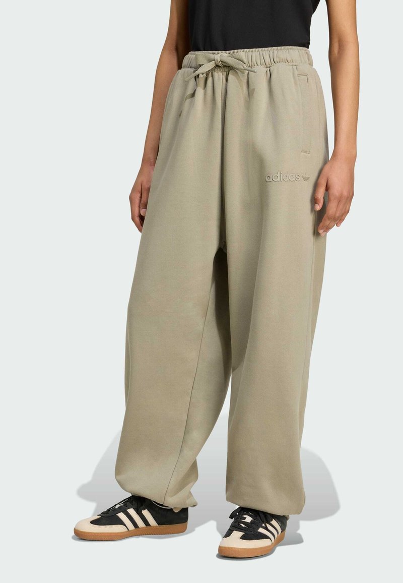 Større beige joggers med snoretræk i taljen, sidelommer og subtil "adidas" broderi, parret med sorte og cremefarvede sportssko.