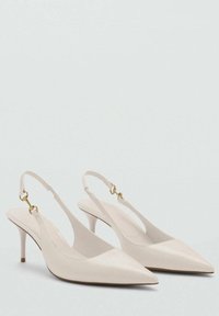 Beige slingback heels with a pointed toe, slim heel, and a single strap featuring gold hardware accents. Smooth texture and streamlined design.