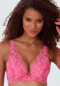 Sutiã de renda rosa com bordas recortadas e padrão floral. Apresenta um decote em V profundo, alças ajustáveis e um detalhe de laço central.