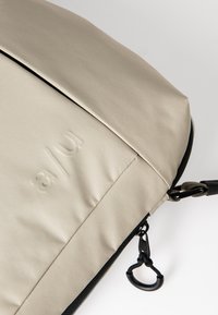 Beige gevoerde laptoptas van textiel met een zwarte rits en een bevestigde clip. Voorzien van een reliëflogo-detail.