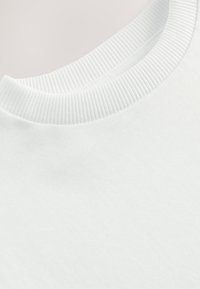 Gros plan d'un col rond blanc avec une texture en maille côtelée et un tissu en coton lisse sur le corps d'un vêtement.