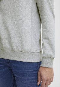 Light gray sweatshirt with ribbed cuffs and hem, featuring a soft texture and side seam details, paired with dark blue jeans.