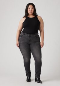 Zwarte geribbelde bodysuit gecombineerd met donkere skinny jeans en zwarte blokhakken, met een klassieke vijf-pocket ontwerp en subtiele vervagingdetails.