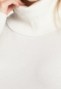 Witte geribde turtlenecktruien met een strakke pasvorm, voorzien van een zachte textuur en een hoge geribde kraag, benadrukt schone lijnen en eenvoud.
