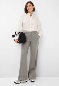 Lichte, knoopsluiting, witte shirt met lange mouwen; grijze, wijde broek met zakken; zwarte tas; zilveren sportschoenen met mesh accenten.
