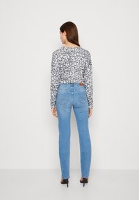 Top de manga larga con estampado de leopardo en gris y blanco, combinado con jeans ajustados de tiro alto en azul claro, que cuentan con bolsillos traseros y un acabado suave.