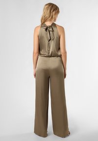 Olijfgroen satijnen jumpsuit met halternek, gestrikt strikdetail op de rug, wijde pijpen, met een soepele textuur en een relaxte pasvorm.