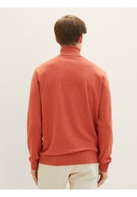 Pull en col roulé couleur rouille avec des poignets et un ourlet côtelés. Texture tricotée, coupe décontractée, couleur unie, sans motifs ni embellissements.