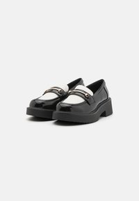 Zwarte gepatineerde leren loafers met een dikke zool, voorzien van een witte lederen strap en gouden hardware accenten. Gladde afwerking met een lichte glans.