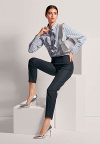 Gestreifte, gerüschte Bluse in Blau und Weiß, kombiniert mit maßgeschneiderten schwarzen Hosen und silbernen High Heels. Enthält eine silberne Handtasche.