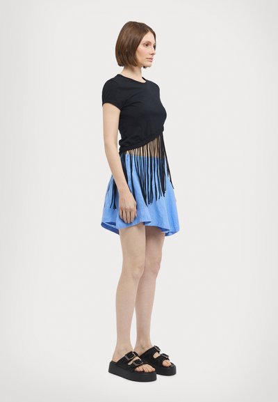 Haut noir à manches courtes avec des détails en frange, associé à une jupe patineuse bleu clair. Sandales à plateforme noires avec des boucles.