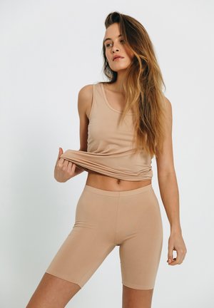 Beige tank top og matchende shorts lavet af blødt, strækbart stof. Toppen har en rund halsudskæring, og shortsene er tætsiddende og går til midt på låret.
