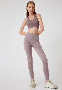 Licht paarse, gestructureerde workout set met een aansluitende crop top en high-waisted leggings. Sneakers met crème en beige accenten maken de look compleet.
