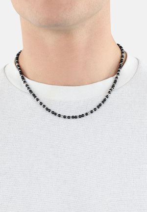 Black and silver beaded necklace featuring alternating spherical beads, worn above a white textured shirt with a round neckline.