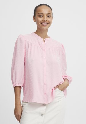 Pink button-up blouse with textured dots, relaxed fit, 3/4 puff sleeves, and a curved hem, paired with a light-colored skirt.