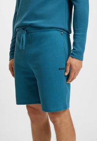 Blauwe textuurshorts met een elastische tailleband, trekkoord en een klein zwart logo aan de zijkant. Geschikt voor casual of sportieve kleding.