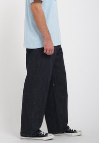 Ciemne spodnie dżinsowe o szerokich nogawkach z teksturowanym wykończeniem, zestawione z jasnoniebieskim bawełnianym t-shirtem i czarnymi tenisówkami z płótna.