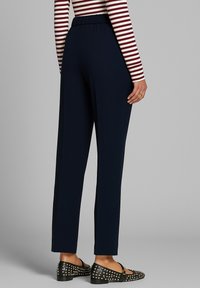 Pantaloni blu navy a gamba larga con vita elastica, texture liscia e vestibilità rilassata. Abbinati a ballerine nere con borchie.