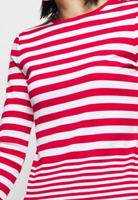 Czerwona i biała w paski koszula z długim rękawem, z okrągłym dekoltem i gładką bawełnianą tkaniną. Paski są równomiernie rozmieszczone i mają intensywny kolor.