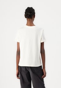 Weißes Baumwoll-T-Shirt mit umgeschlagenen kurzen Ärmeln und rundem Hals. Die Rückansicht zeigt eine bequeme Passform und eine glatte Textur. Kombiniert mit dunklen Hosen.