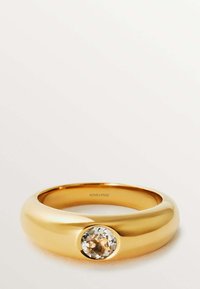 Anillo de oro con una banda suave y redondeada y una gema clara central engastada en un bisel. Diseño minimalista con acabado pulido.