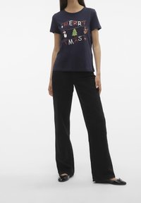 Námořnické tričko s potiskem "MERRY CHRISTMAS" a svátečními ikonami; kombinováno s černými širokými kalhotami a černými plochými botami. Bavlněný materiál.