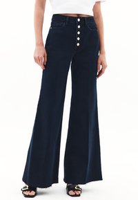 Spodenki dżinsowe o szerokich nogawkach w ciemnoniebieskim kolorze, z wysokim stanem i zapięciem na pięć guzików, z kieszeniami z przodu i surowymi końcami.
