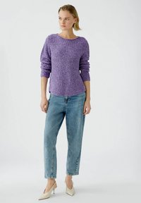 Lila gestrickter Pullover mit langen, puffigen Ärmeln und Rundhalsausschnitt, kombiniert mit hellblauen, locker geschnittenen Jeans und cremefarbenen High Heels.